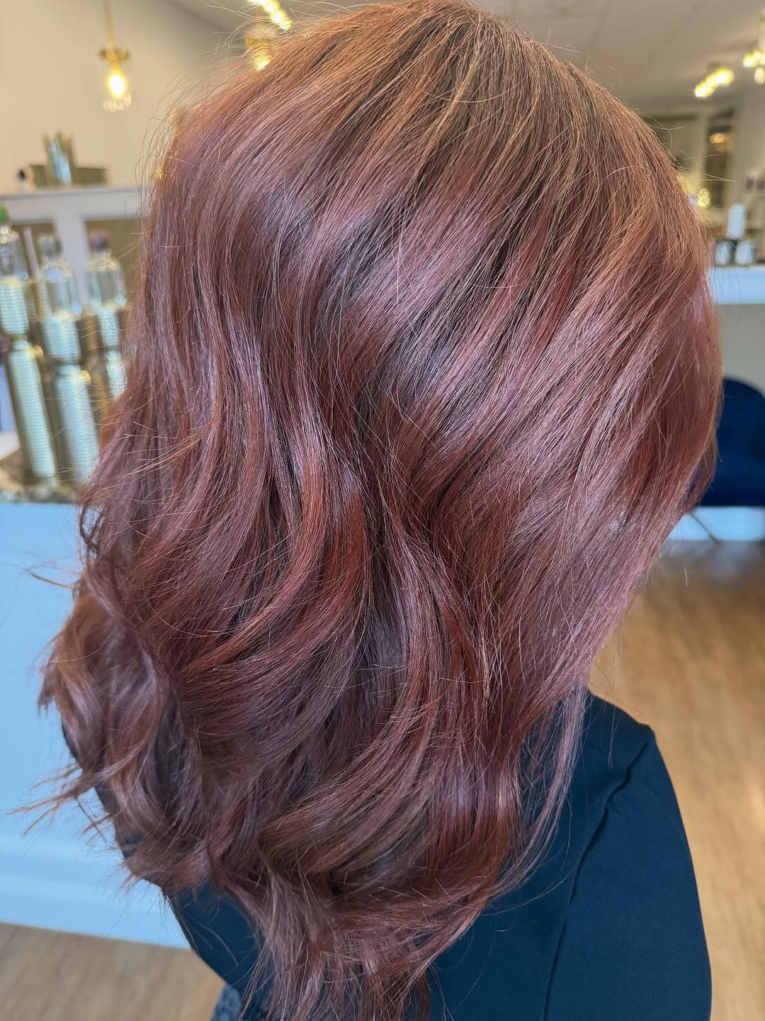 Back view of a woman's shoulder-length hair with burgundy-red highlights and soft waves in a salon setting.